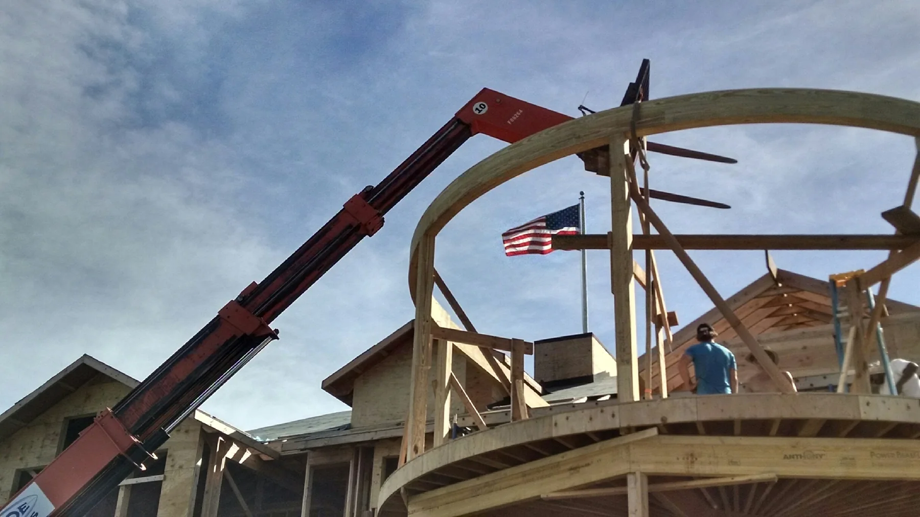 Curved beam framing lifted into place with an American flag visible on site
